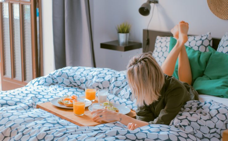 woman laying on bed in hotel room eating breakfast
